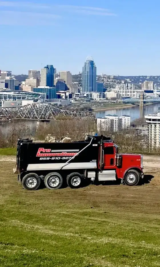 Pro Innovations dump trucks on a graded hilltop above the Cincinnati skyline
